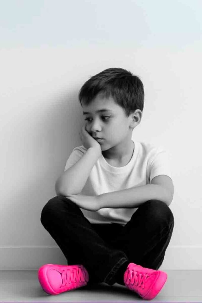 Niño sentado solo en el suelo con gesto pensativo sin juguetes ni pantallas Fondo blanco estética minimalista